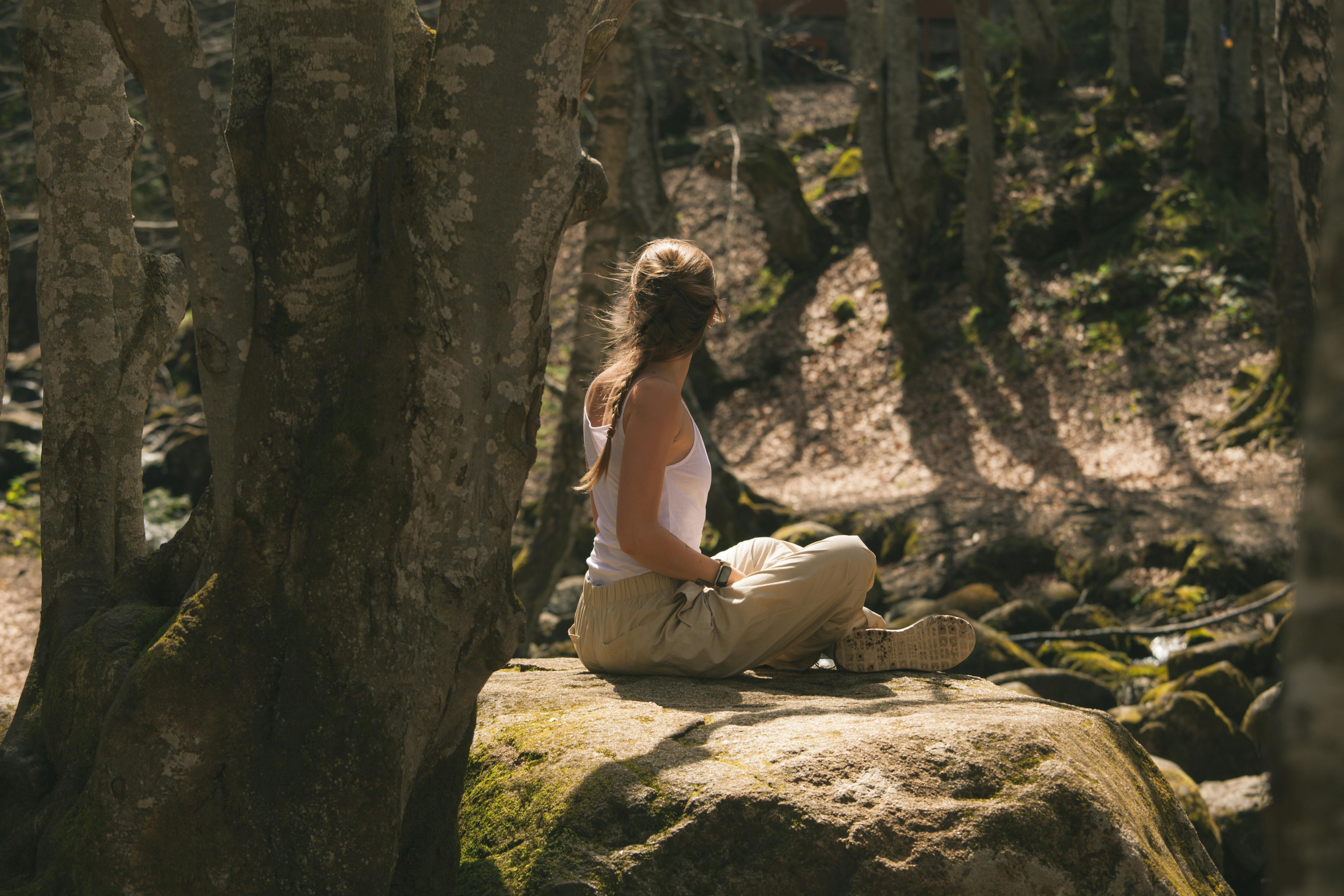 Meditáló résztvevő egy erdei sziklán, napsütésben